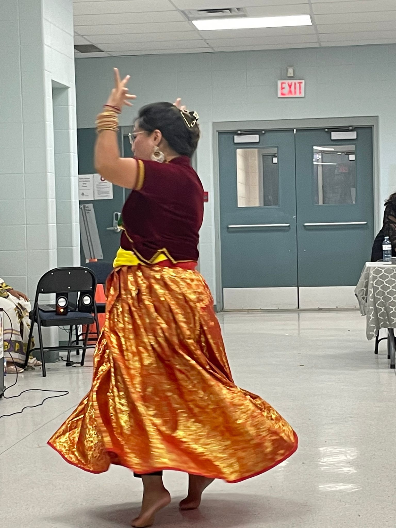 A dancer in wearing a gold colored skirt and red blouse doing a cultural dance.