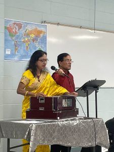 A woman playing an instrument while a man holds a mic to support her.