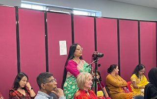 A table with several people watching an event, with Mitali holding a camera with a tripod.