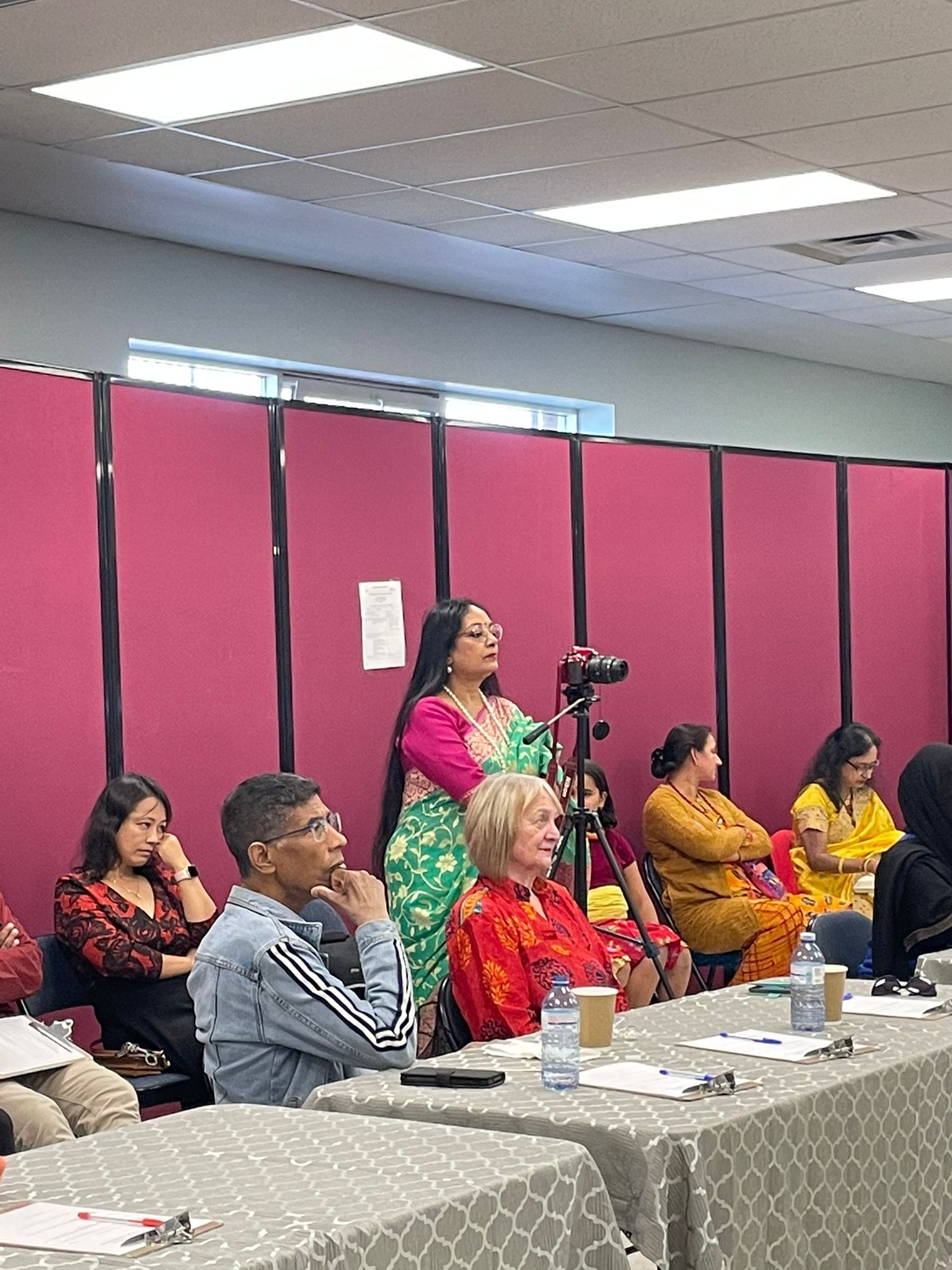 A table with several people watching an event, with Mitali holding a camera with a tripod.